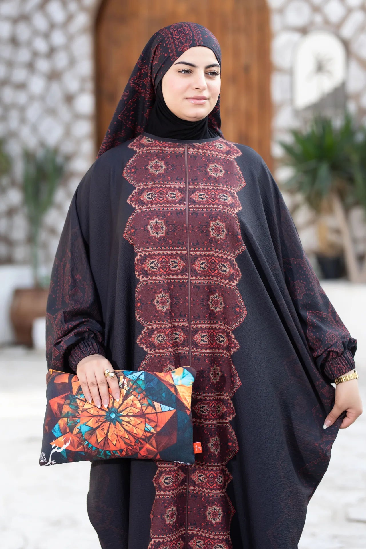 Woman wearing a dark patterned outfit with a colorful clutch bag outdoors.