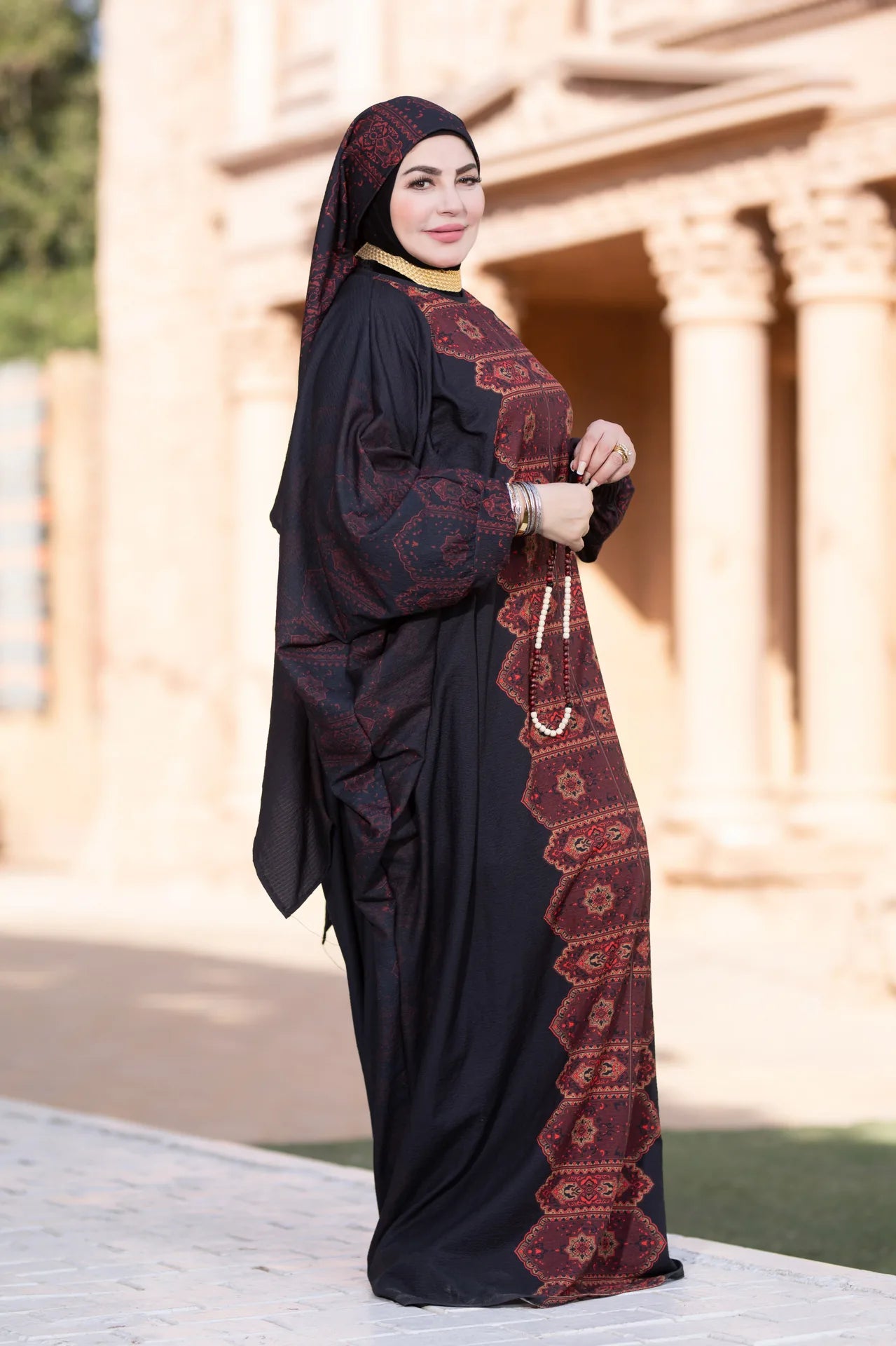Woman wearing a black abaya with red embroidery standing outdoors.