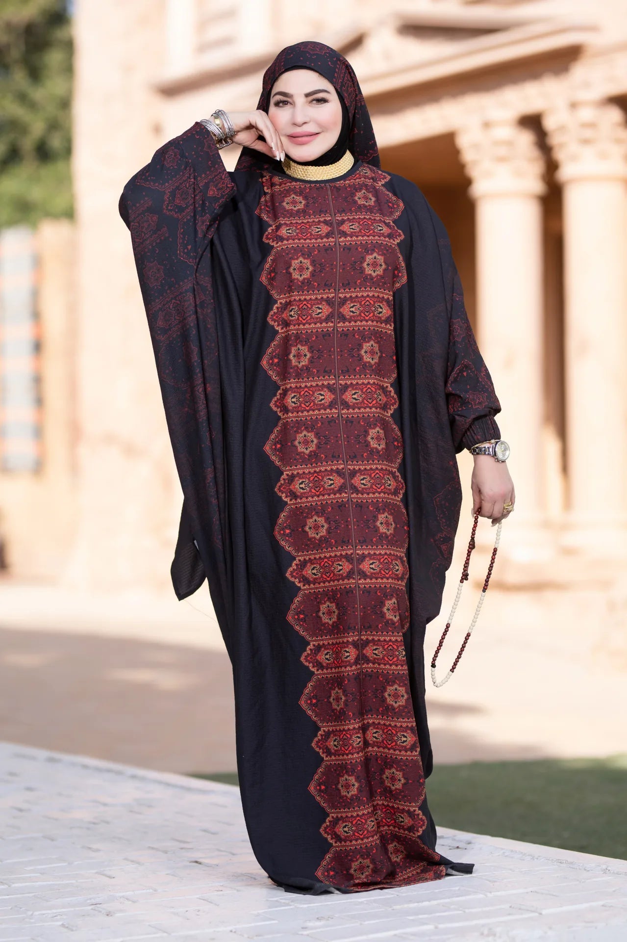 Woman wearing a black abaya with red patterns in an outdoor setting