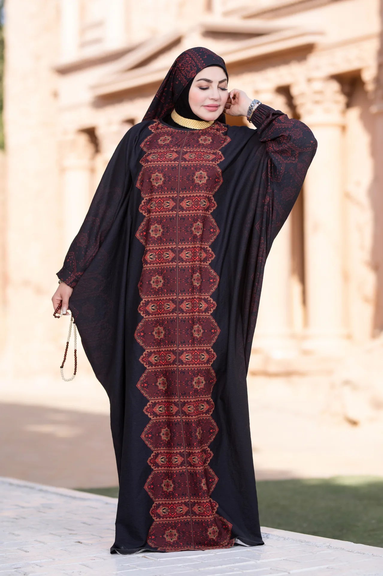 Woman wearing a black abaya with red patterns in an outdoor setting
