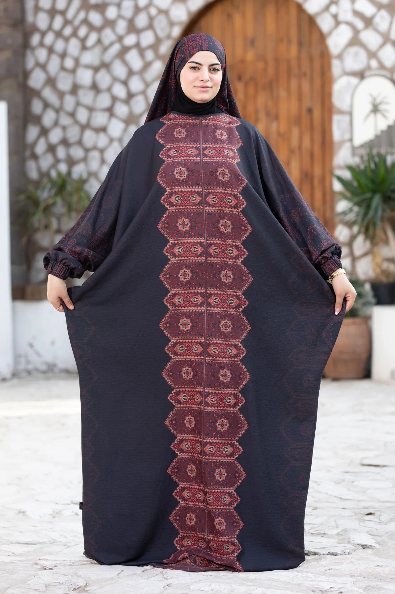 Woman wearing a black abaya with red embroidery in an outdoor setting.