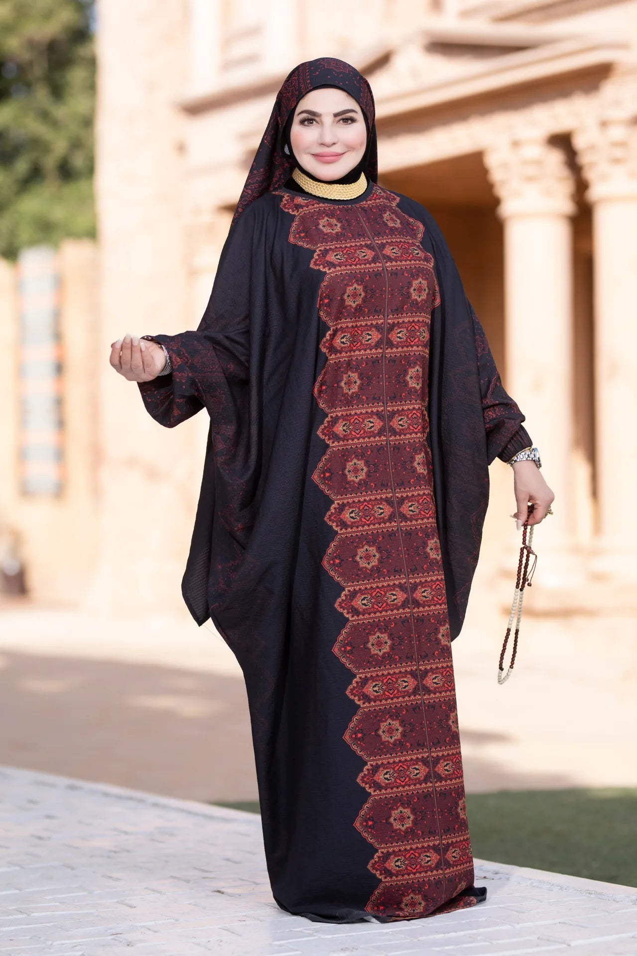 Woman wearing a black abaya with red patterns in an outdoor setting