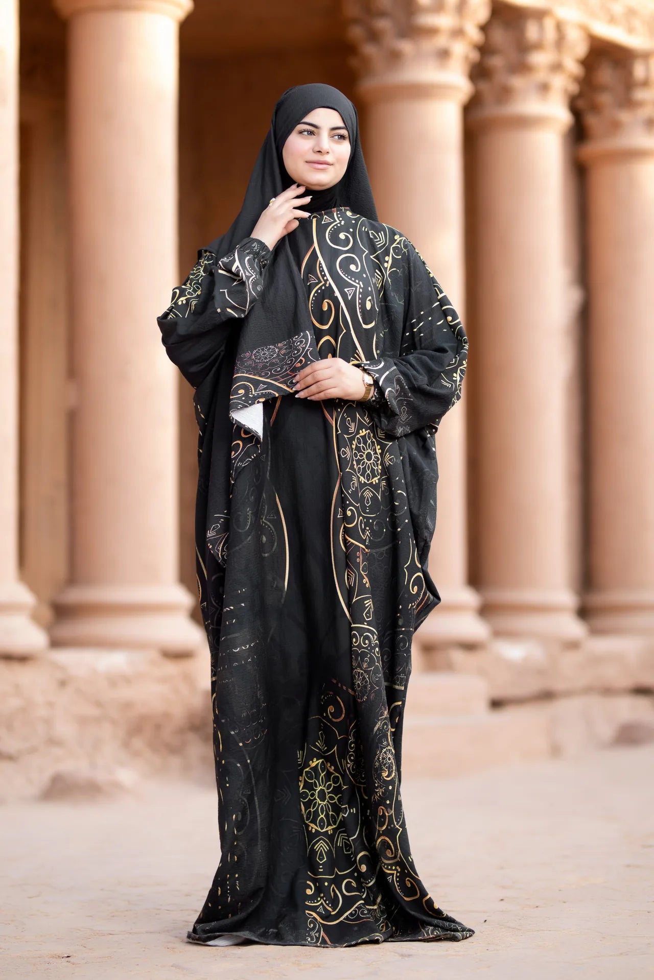 Woman wearing a black abaya with gold embroidery in front of architectural columns.