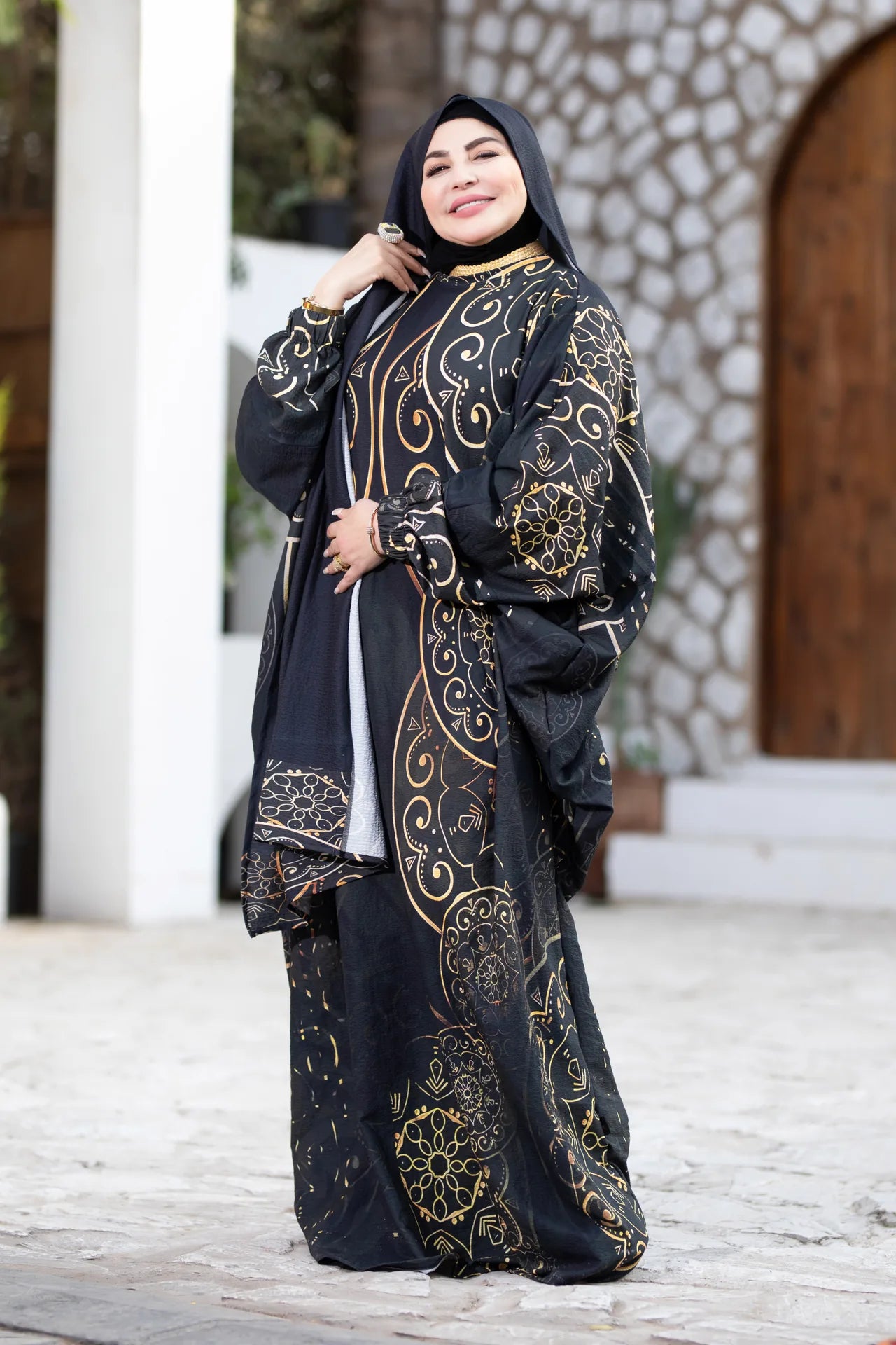 Woman wearing a black and gold embroidered abaya in an outdoor setting.