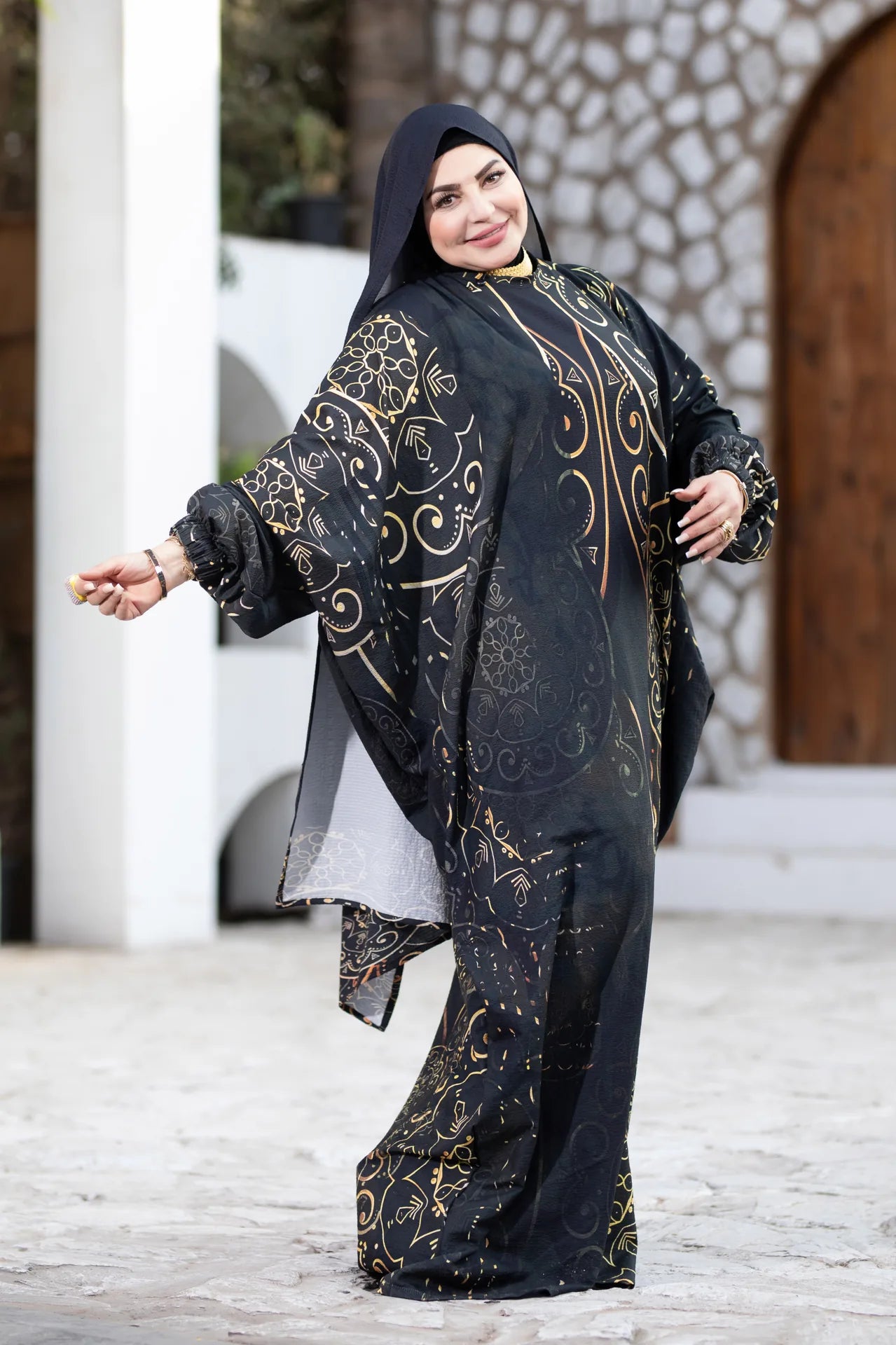 Woman wearing a black and gold traditional outfit with a stone wall background