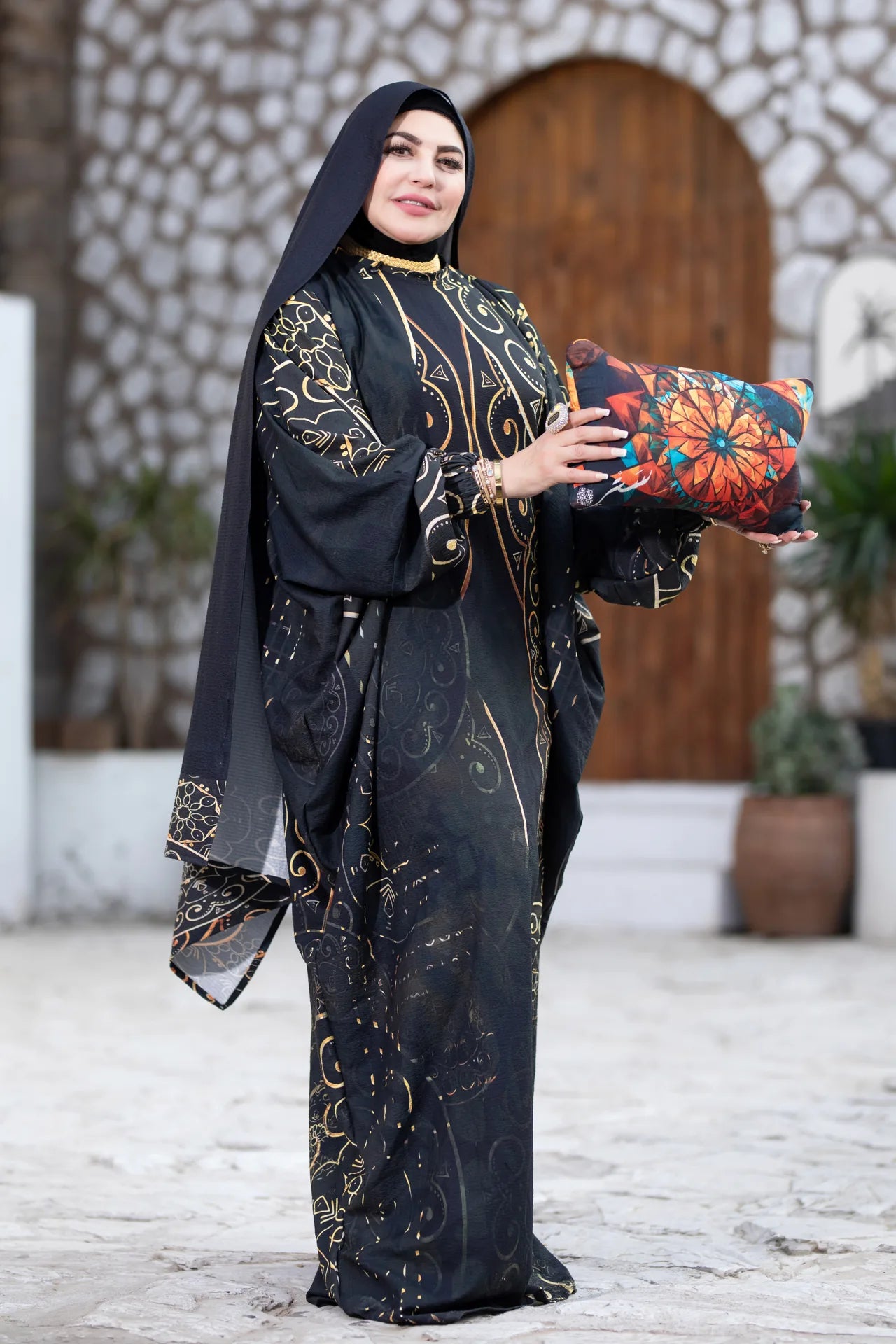 Woman in traditional black and gold outfit holding a colorful bag in an outdoor setting.