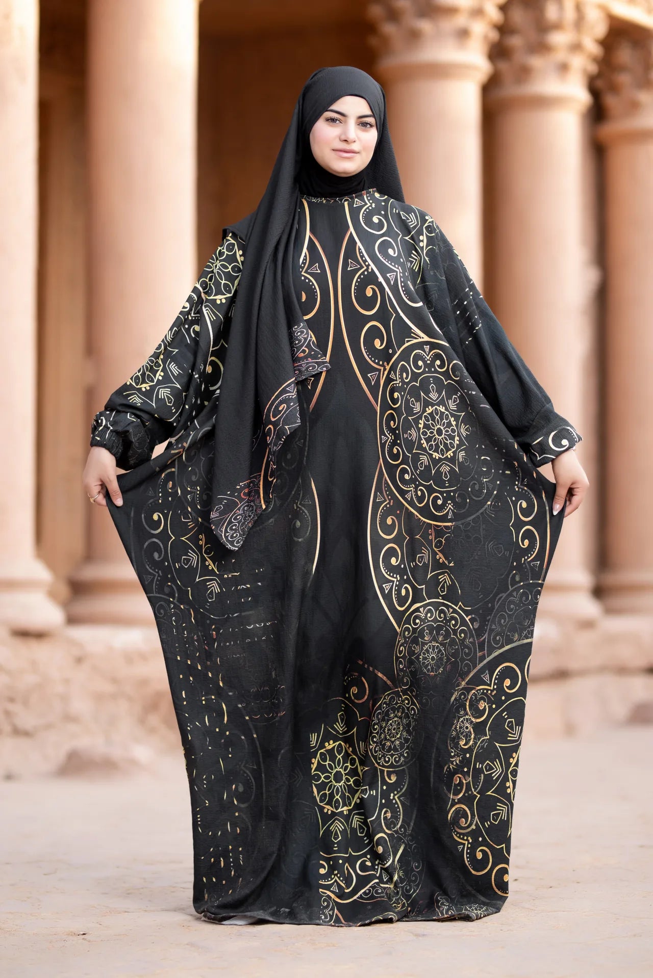 Woman wearing a black abaya with gold embroidery in front of classical architecture.