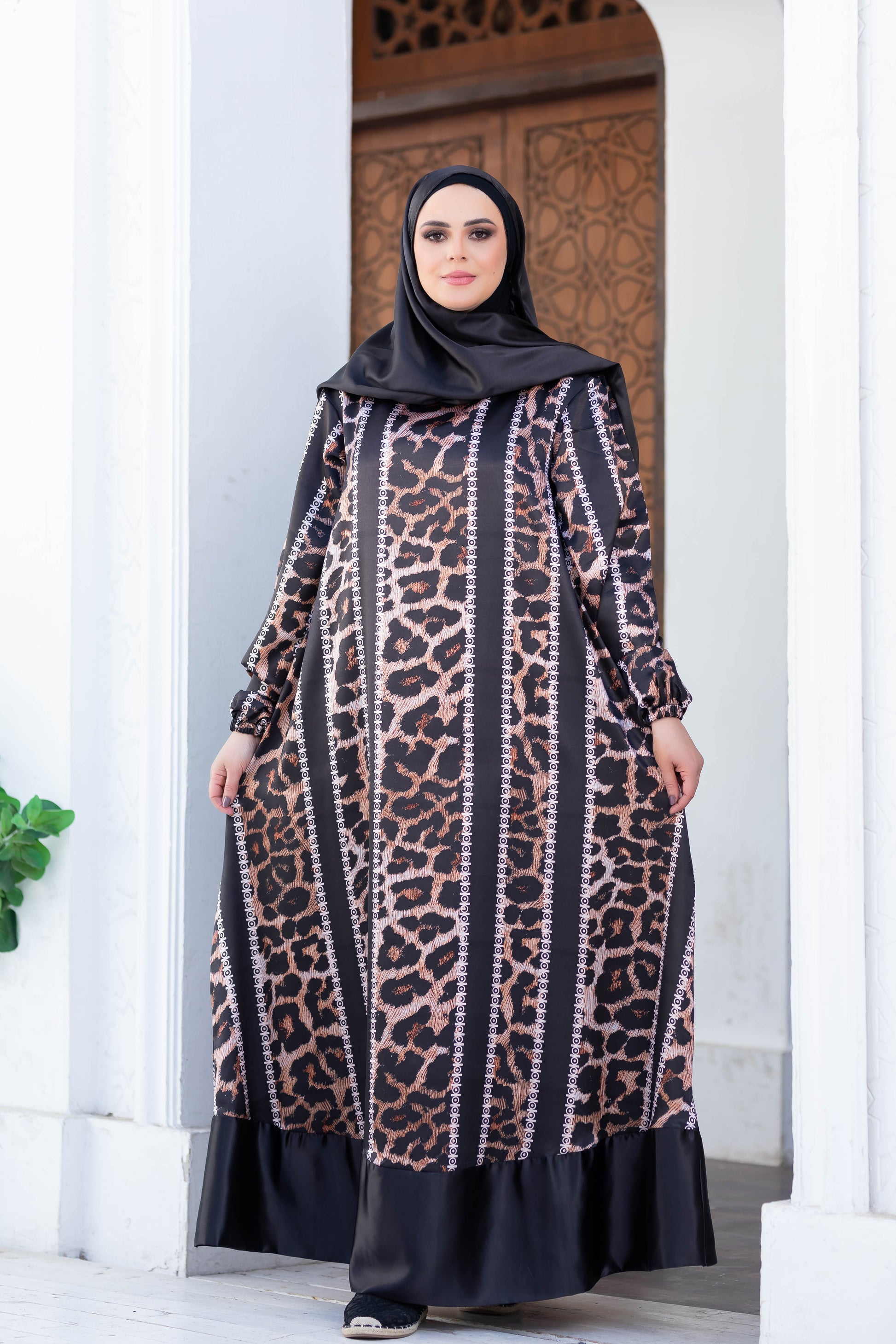 Elegant leopard print maxi dress featuring a modest hijab, worn by a woman standing in front of an ornate doorway.