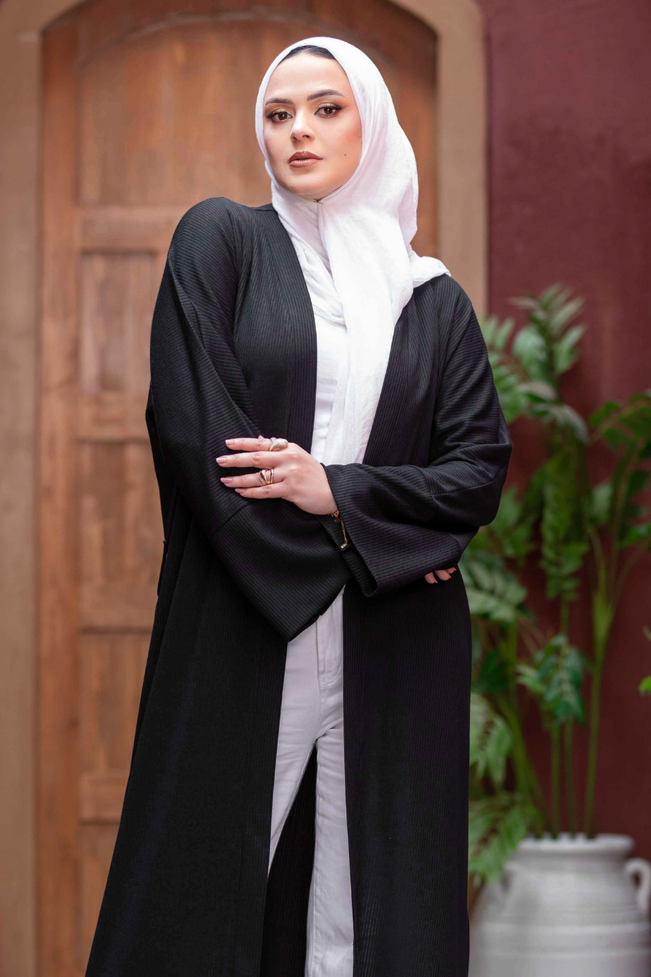 Elegant black kimono with wide sleeves, worn by a woman in a traditional Islamic headscarf, standing in an outdoor setting with architectural details.