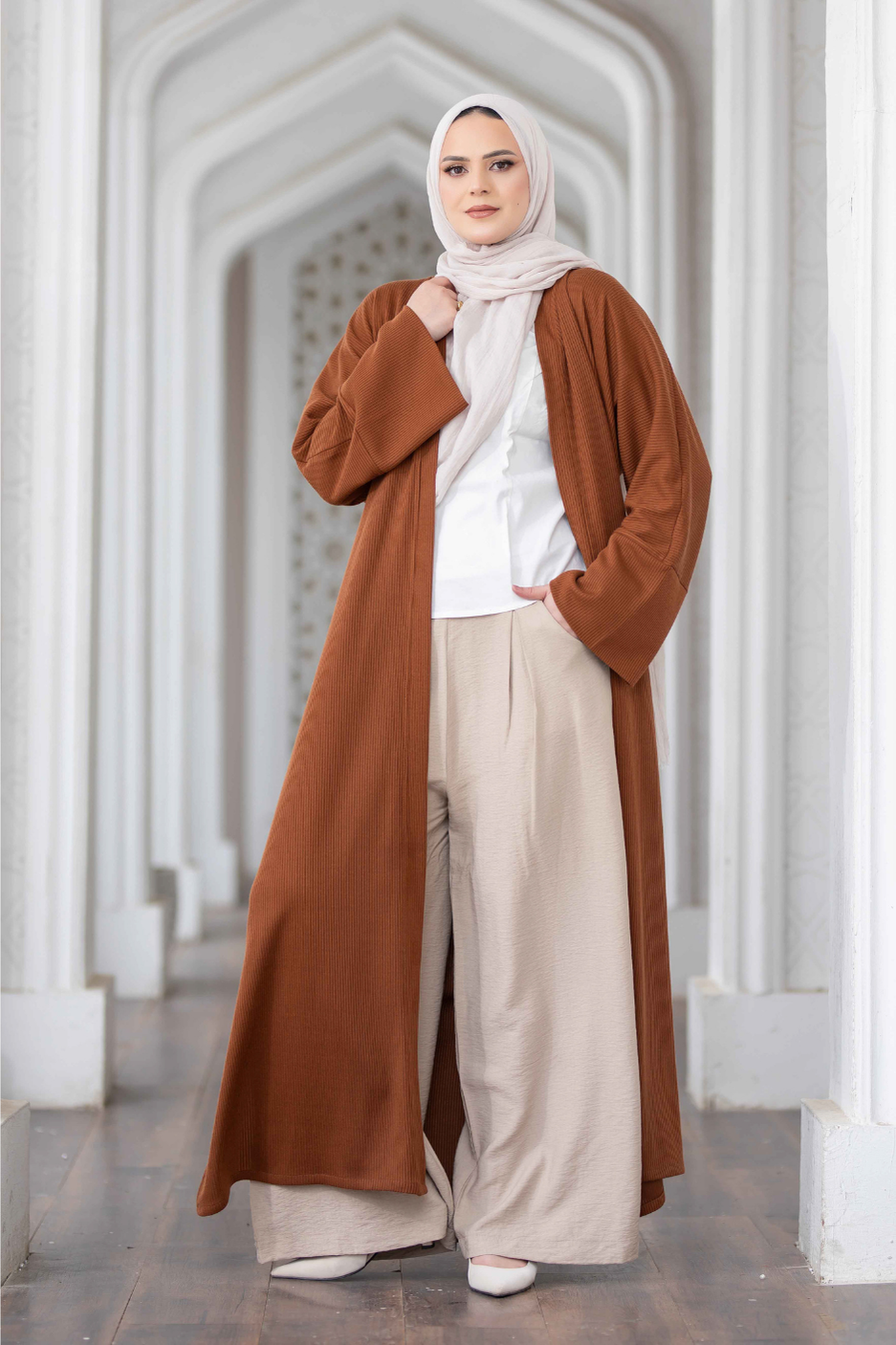 Elegant long brown kimono with wide sleeves, worn by a woman in a traditional Islamic headscarf, standing in a modern architectural setting.