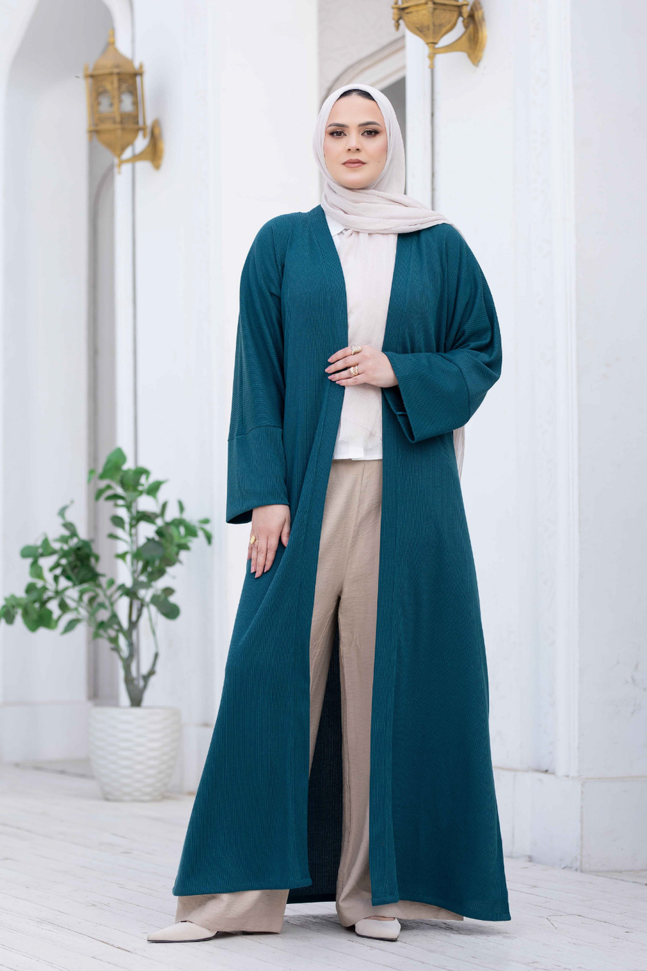 Elegant teal kimono with wide sleeves, worn by a woman against a white wall with decorative lighting fixtures.