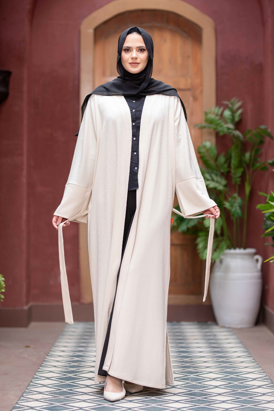 Elegant cream-colored kimono with wide sleeves, worn by a woman with a black hijab, standing in front of a red brick wall.