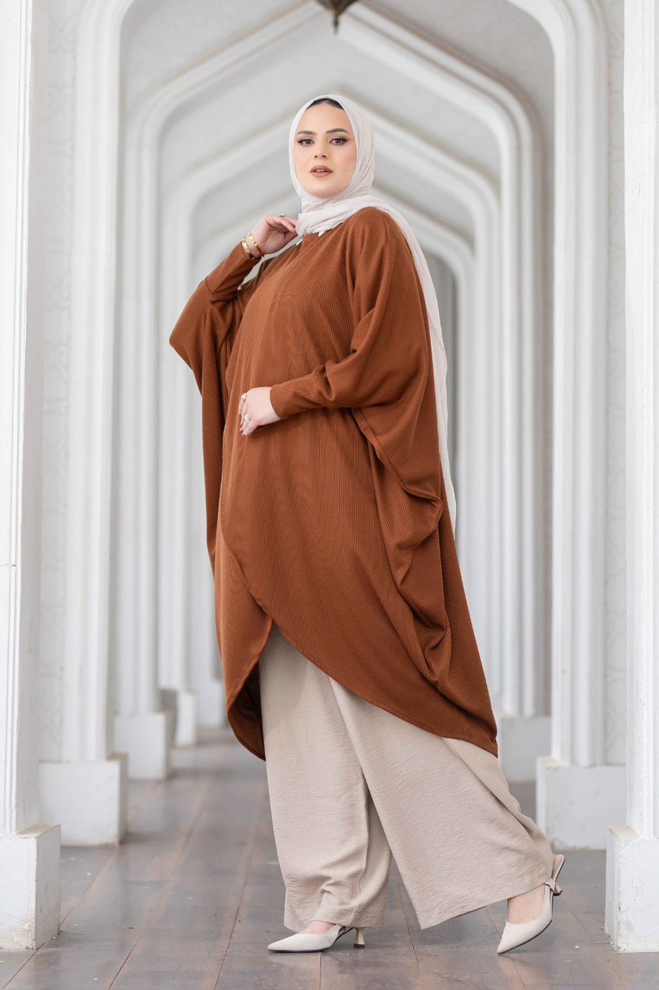 Elegant brown cardigan and flowing off-white pants worn by a fashionable woman in a white architectural setting