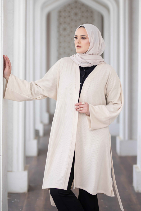 Elegant wool blend midi coat for women in neutral tone, with female model wearing hijab presented against ornate architectural background.