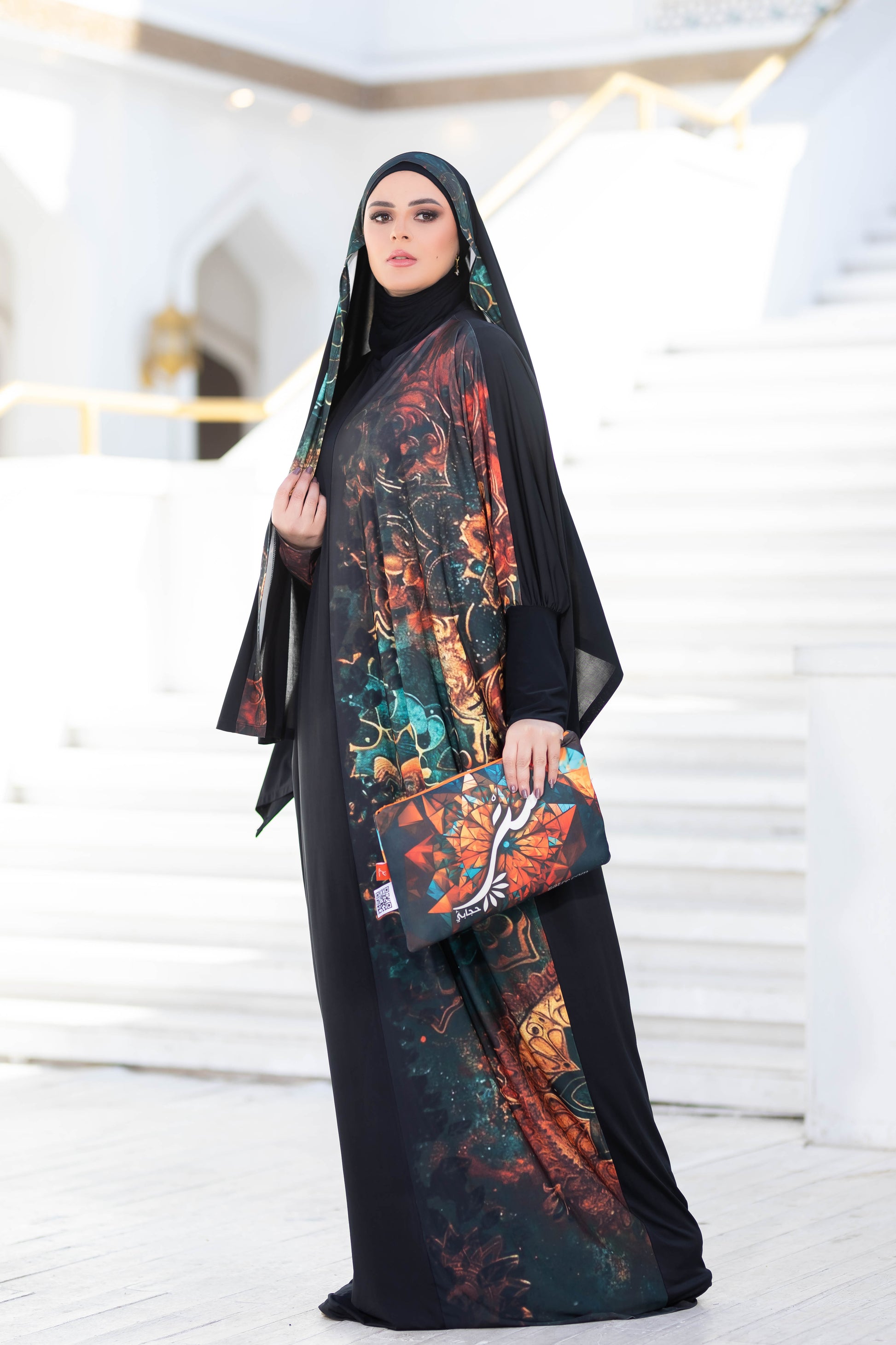 Modest Isdal 777172 - Traditional multi-colored floral print abaya with black hijab, worn by a young woman in an indoor setting.