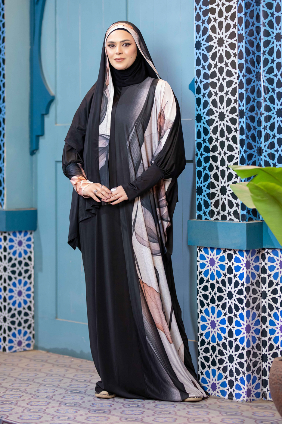 Black and grey striped modest abaya worn by woman against patterned tile wall