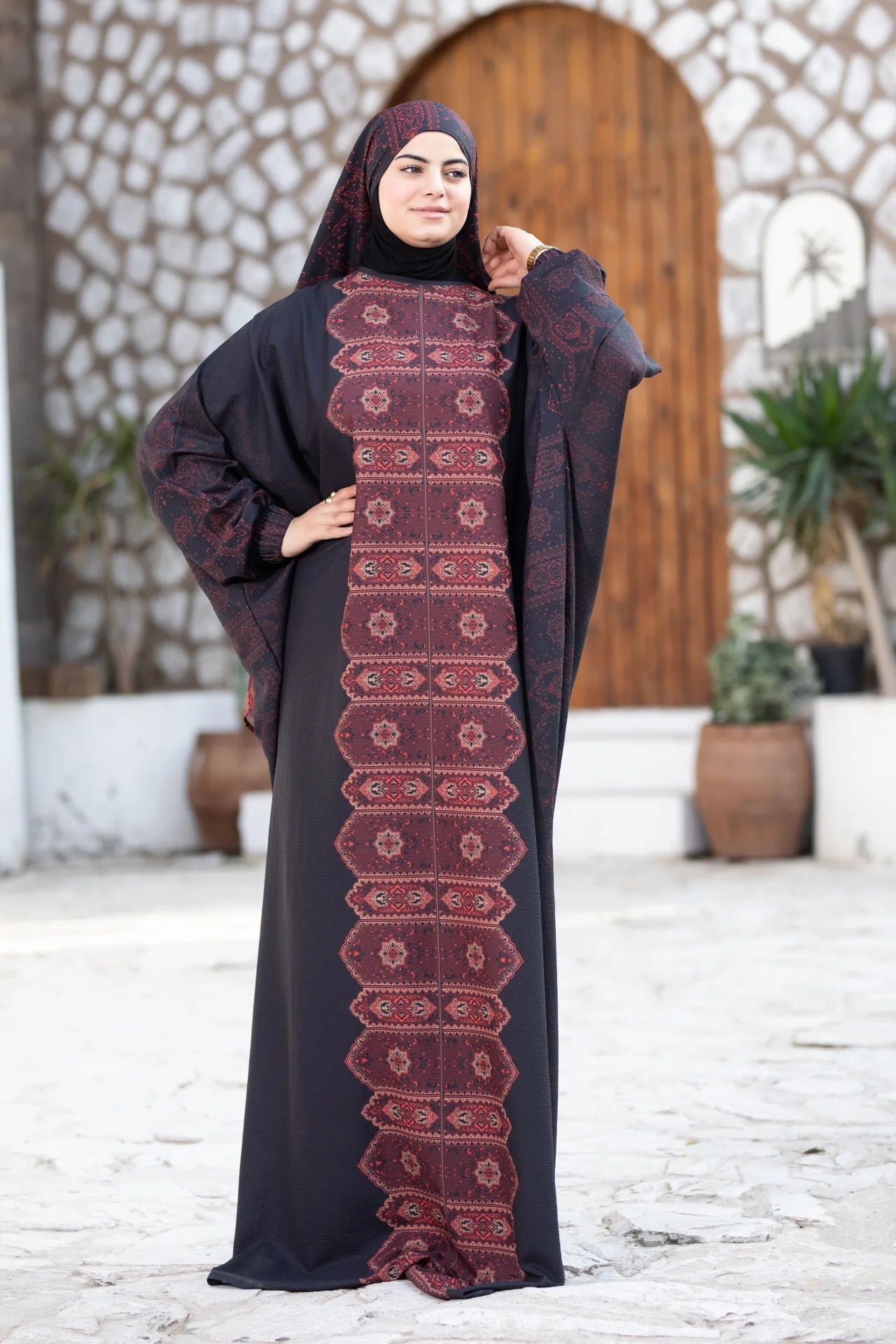 Woman wearing a black abaya with red embroidery in an outdoor setting.
