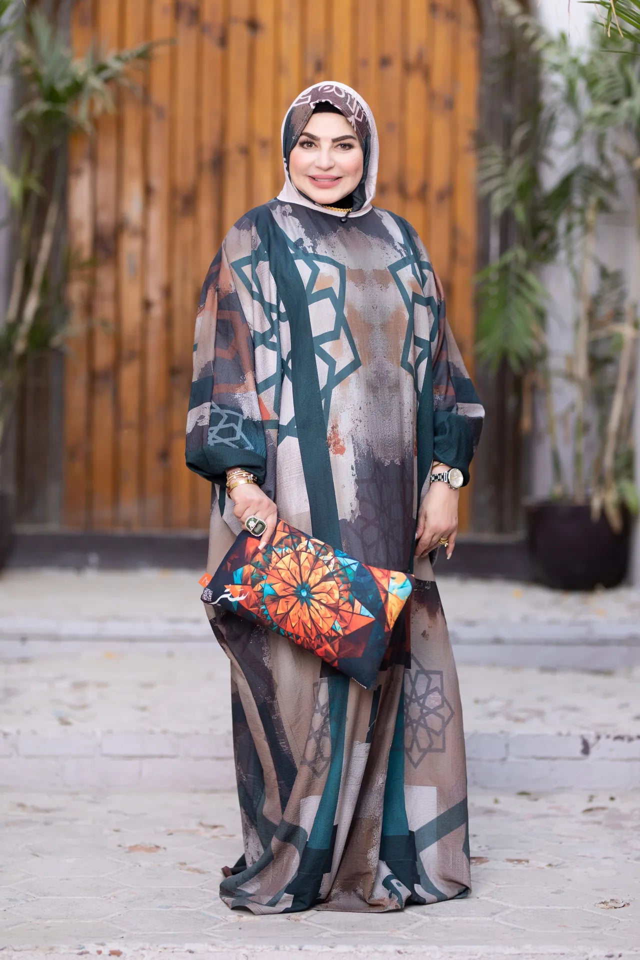 Woman in a patterned outfit with a floral clutch standing outdoors.