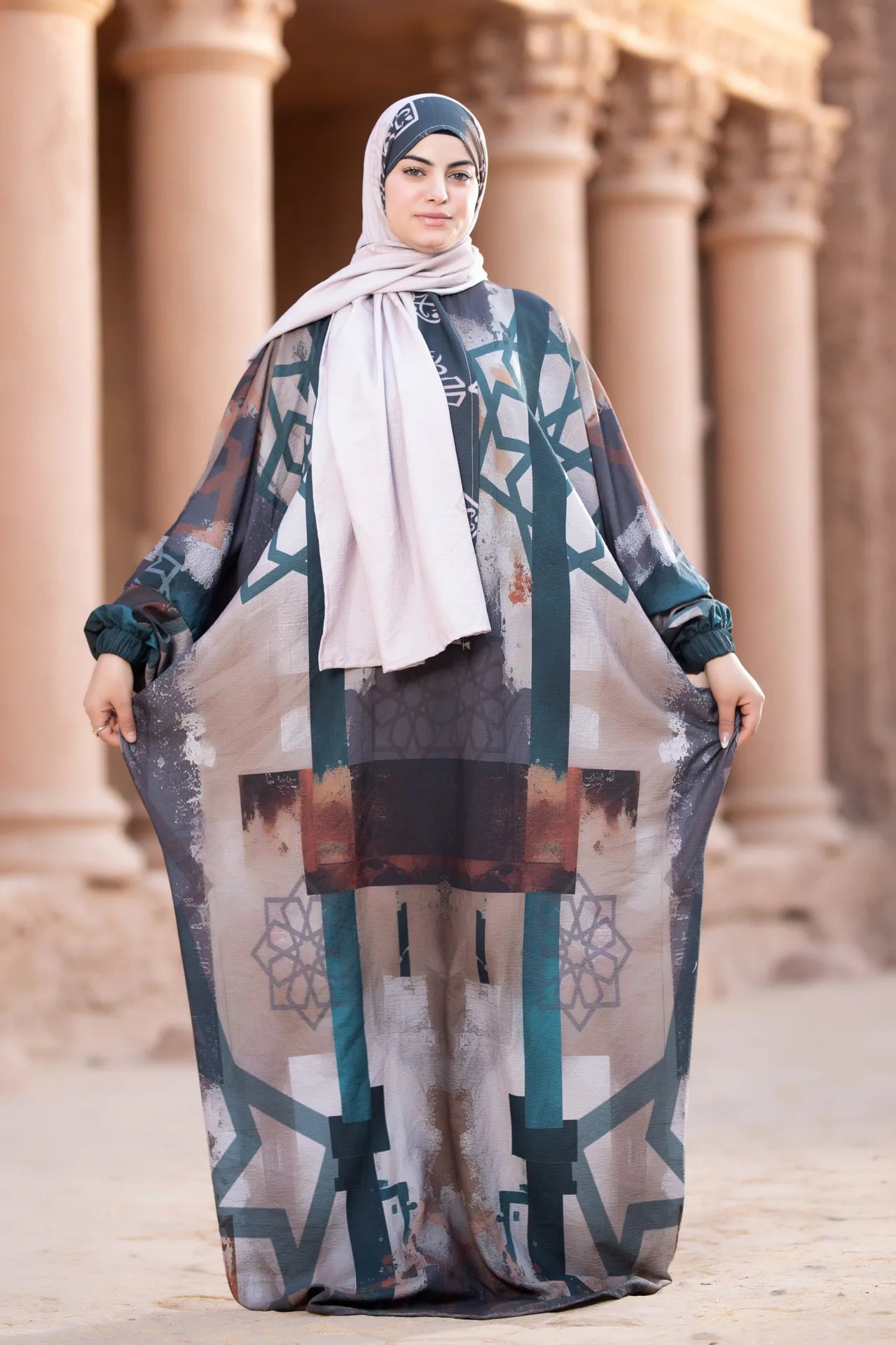 Woman wearing a patterned dress and hijab in front of classical architecture