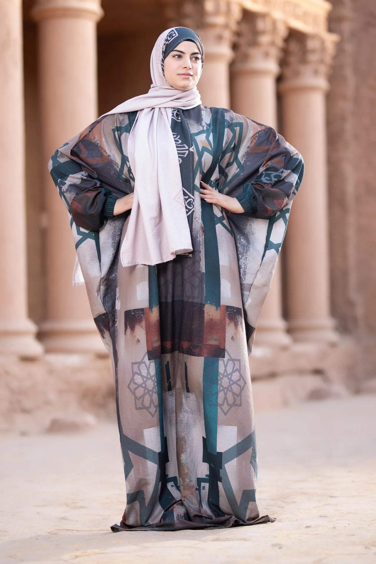 Woman wearing a patterned abaya and hijab standing in front of architectural columns.